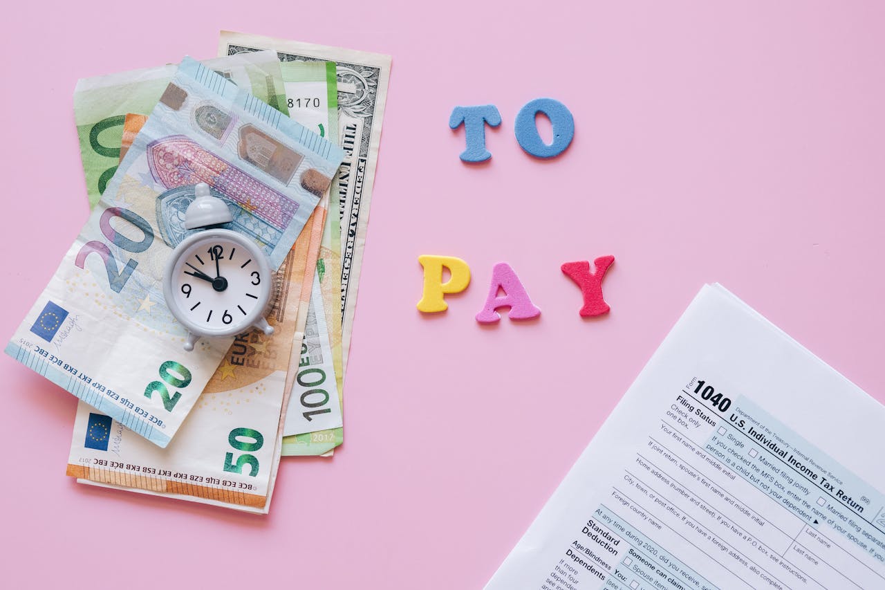 Flat lay of taxes, currency, and reminder to pay on pink background.